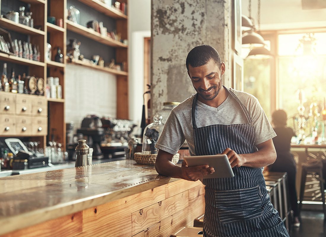 Business Insurance - Portrait of a Young Small Business Owner Leaning Against the Bar in his Restaurant While Using a Tablet