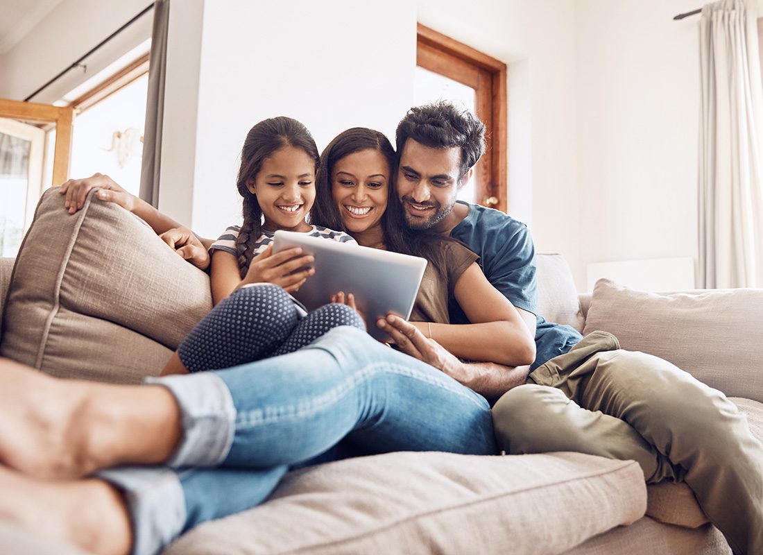 Current Clients - Portrait of a Cheerful Famiily with a Young Daughter Spending Time Together Using a Tablet While Sitting on the Sofa at Home