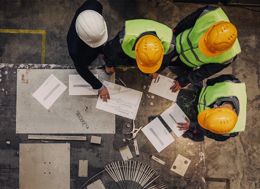 IOI Workers' Compensation - Looking Down at a Small Group of Contractors Standing Around a Table with Blueprints and Charts Discussing a New Construction Project