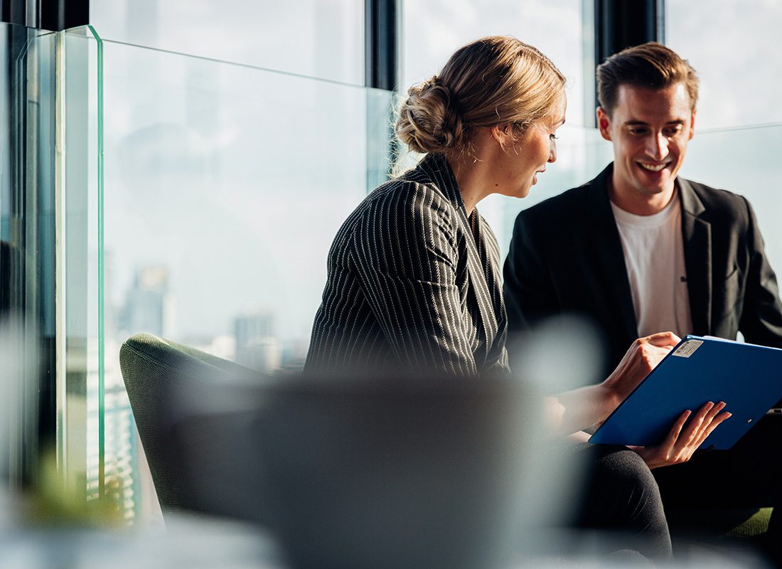 Resource Library - Portrait of a Mature Business Woman Sitting in an Office with a New Young Male Employee Discussing Paperwork