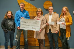 About Our Agency - View of Smiling Synergy Insurance Team Members Handing Over a Check to Volunteers at Camp Ray Bird