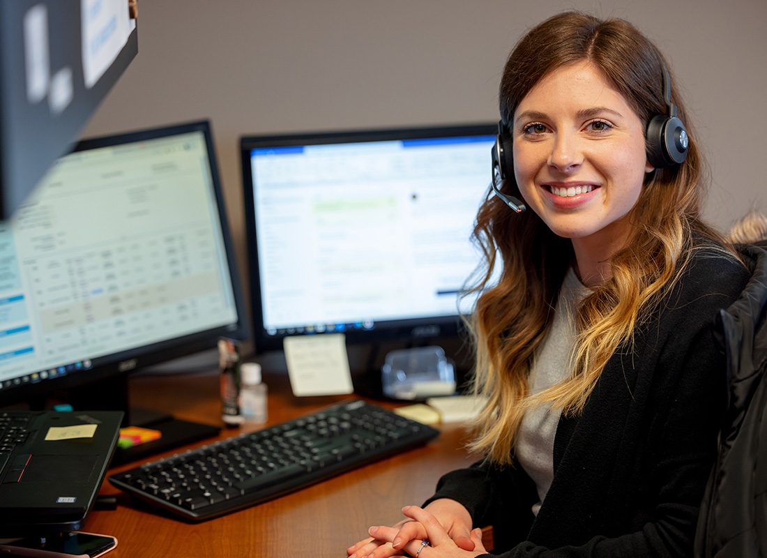 Contact - Closeup Portrait of a Smiling Young Female Employee Wearing a Headset at Synergy Insurance Sitting Behind her Desk at the Office